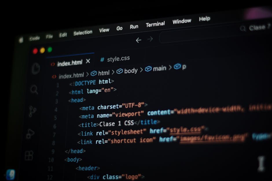 A person working on a laptop with a dark screen displaying lines of code, sitting at a modern table. The laptop has a black keyboard and is slightly open, revealing a vibrant desktop wallpaper and app